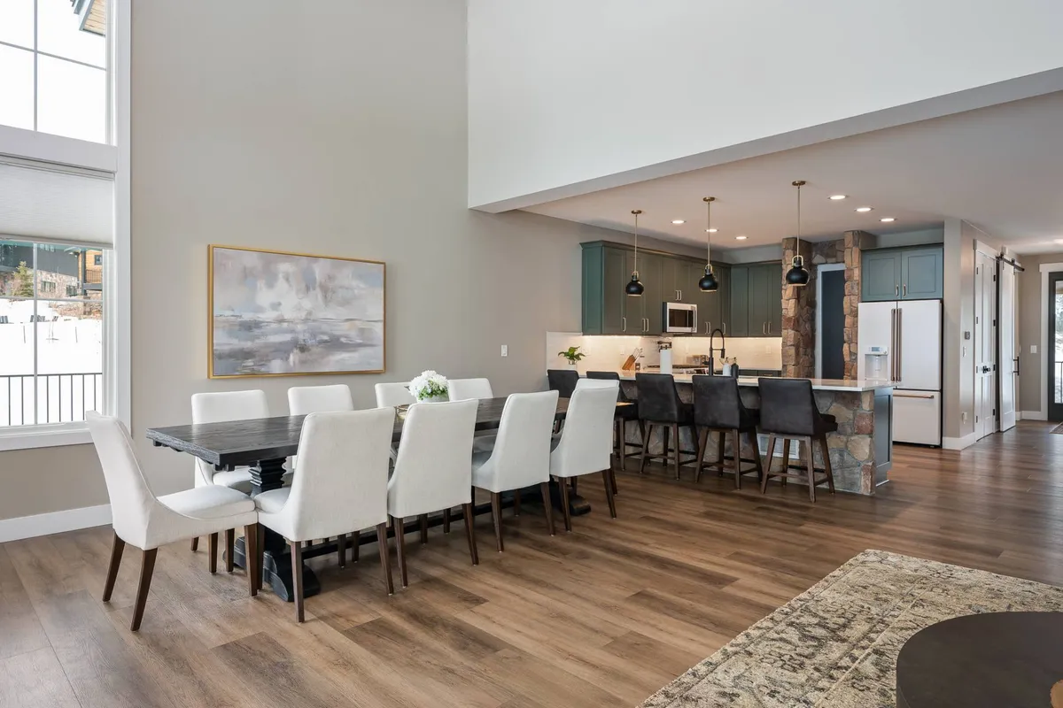 A view of the grand dining table adjacent to the kitchen island, with colorful artwork and pendant lighting adding a festive, welcoming touch. The table is large enough for gatherings and celebrations, emphasizing the social aspect of the dining area.