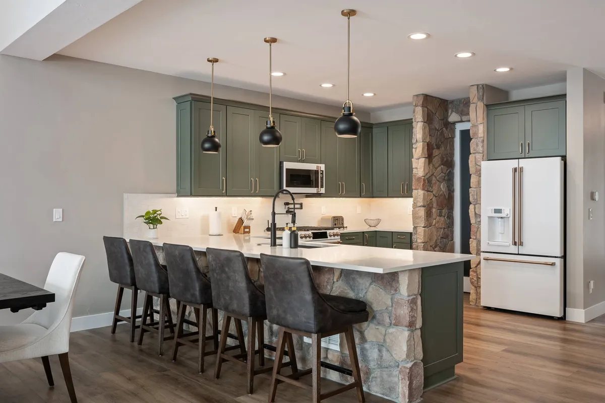 A spacious, modern kitchen featuring a large island with seating, stone accent wall, stylish pendant lighting, and stools. The open layout encourages group cooking, casual dining, and lively conversation, making it a hub for group gatherings.