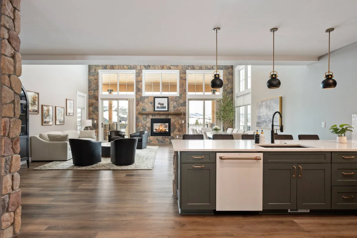 A sophisticated open-plan living area seamlessly blends a spacious kitchen island, modern fireplace, generous seating area, and floor-to-ceiling windows. The layout invites conversation and togetherness, with mountain vistas serving as a captivating backdrop.