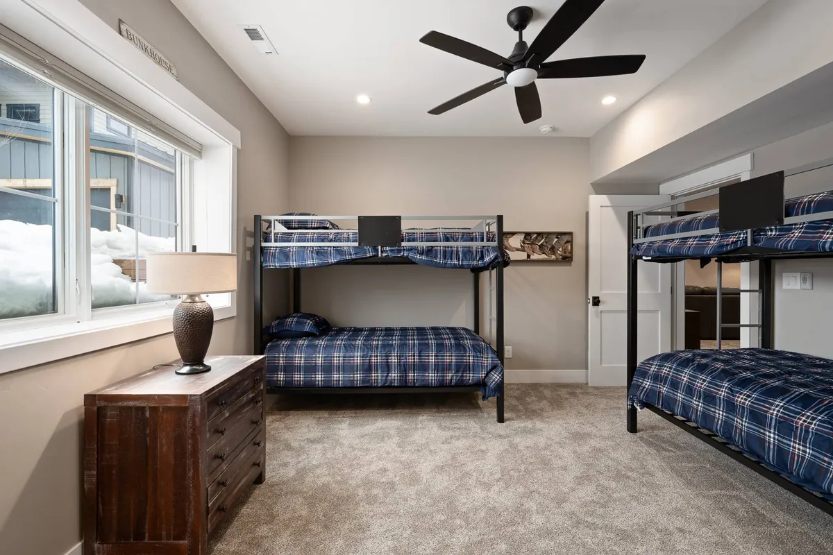 A comfortable flex space with bunk beds, a table lamp, and a window overlooking a snowy landscape, designed to be adaptable for kids’ play, extra sleeping, or quiet relaxation.