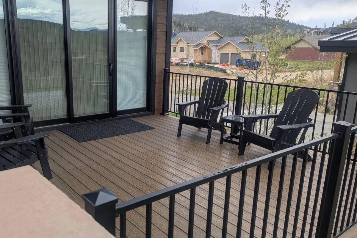 A serene outdoor deck features Adirondack chairs and a striking mountain view, with a wooden railing and easy access to the house via a sliding glass door. The space is perfect for unwinding after a day of games or soaking in sunsets from the bubbling hot tub nearby.