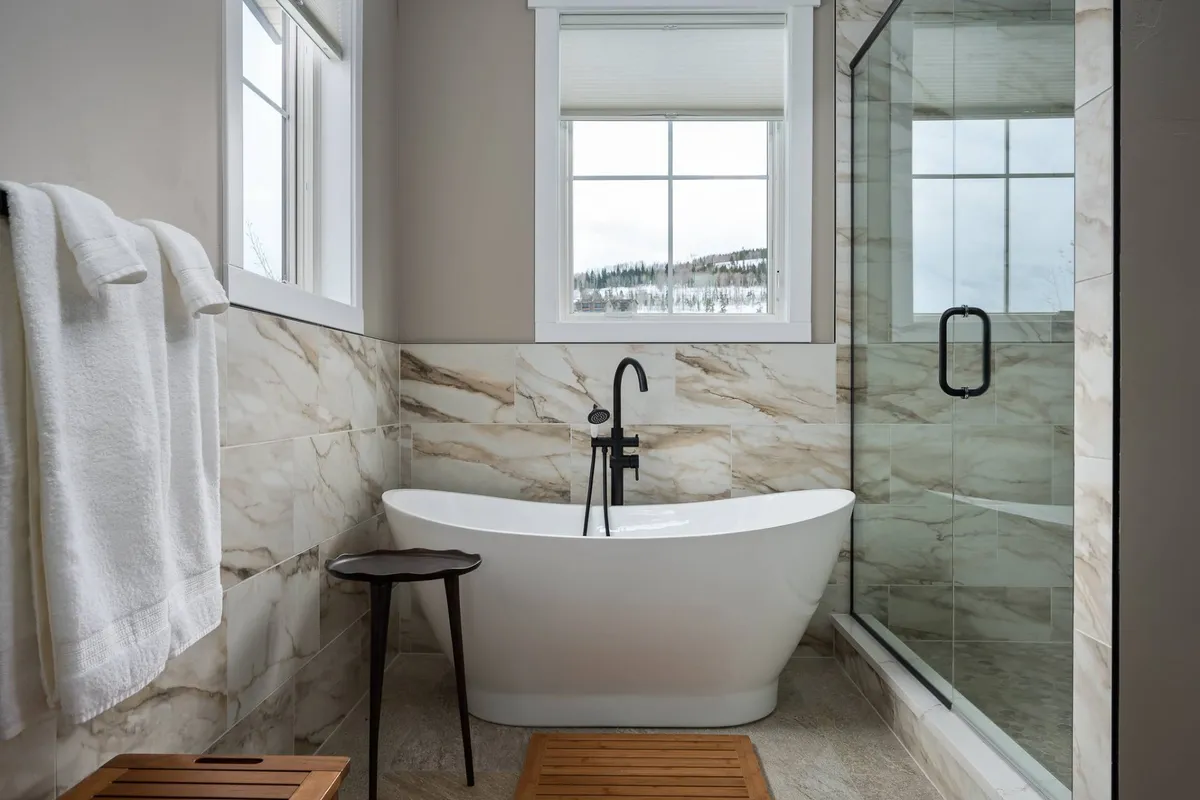 A spa-inspired bathroom with a freestanding bathtub positioned near a large window that floods the space with natural light. The room also features a glass shower enclosure, offering both luxury and practicality.