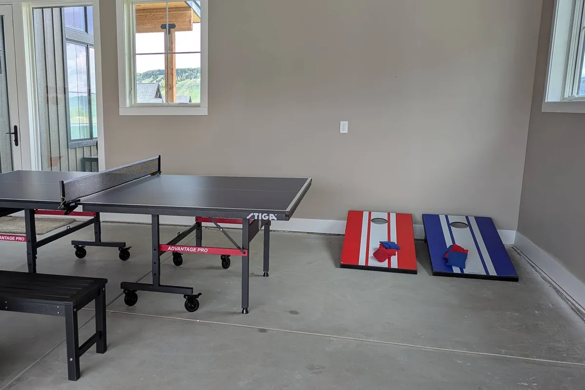 This image captures a vibrant, playful space featuring a ping pong table and cornhole boards—an area designed for friendly competitions and relaxed family fun. The setup highlights the garage's transformation into a game zone, with ample room for movement and socializing.